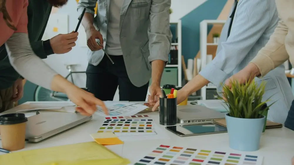A group of people collaborating on a design project at a white office table, illustrating creative AI team management